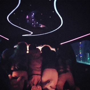 Four people sit in a dark car looking up at a glowing moon-shaped light and stars on the vehicle's ceiling.