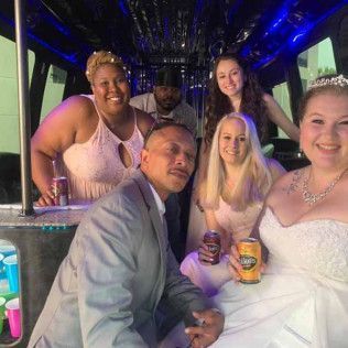 A group of six people smile together inside a decorated party bus, some holding beverages.