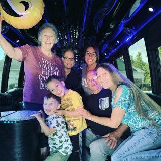 A smiling group gathers inside a limousine, one person holding a yellow balloon.