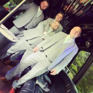 Four people in light-colored suits posing together inside a limousine.