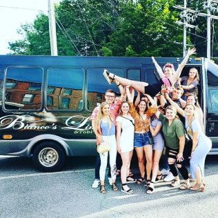 A group of people standing in front of a parked black bus, with one person being held horizontally in the air.