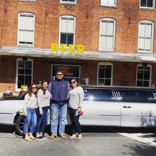 Four people stand in front of a white stretch limousine parked outside a brick building with a yellow 