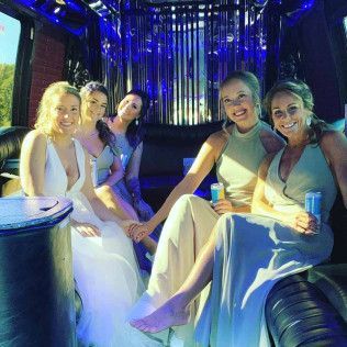 Five people in formal dresses sit together inside a dimly lit limousine with blue accent lighting.