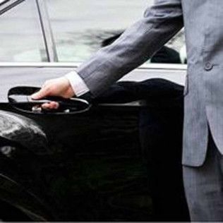 A person in a grey suit jacket opens the door of a black car.
