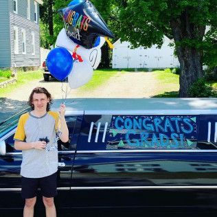 A person holds a graduation balloon bouquet in front of a limousine decorated with a 