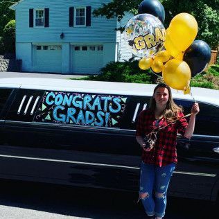 A person holds a bouquet of black and yellow graduation balloons beside a limousine with 