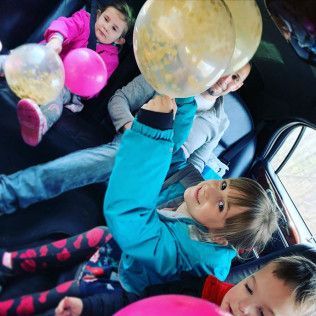 Children and an adult play with balloons inside a car.