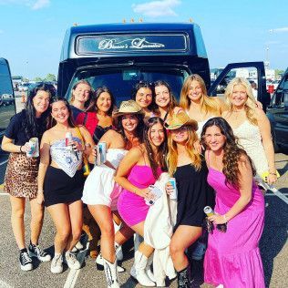 A group of friends posing in front of a shuttle bus in a parking lot, holding beverages and smiling.