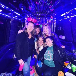 Five people smiling inside a dimly lit limousine decorated with streamers and bathed in blue LED lights.