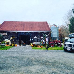 A rustic barn with a red roof, a metal silo, and a red tractor in front, parked on a gravel lot under an overcast sky.