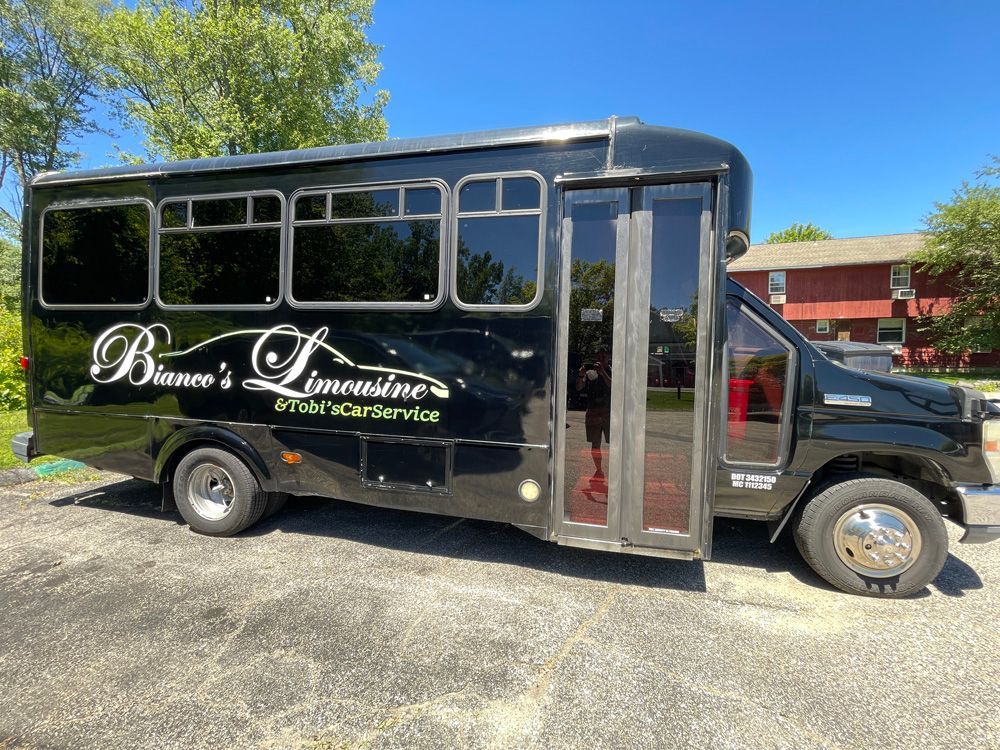A black limousine bus parked outdoors on an asphalt lot with white branding on its side.