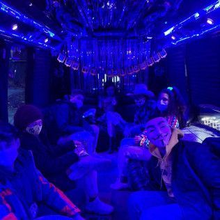 A group of people wearing masks in a party bus illuminated with bright blue neon lights.
