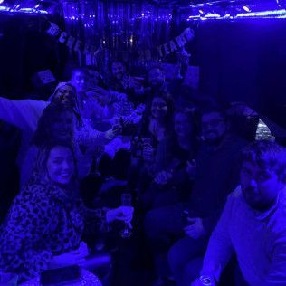 A group of people celebrating at a nighttime party bathed in deep blue lighting, with a banner hanging in the background.