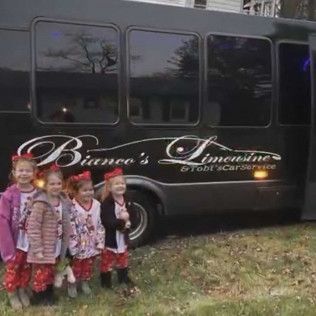 Four children in matching pajamas stand smiling in front of a black Bianco's Limousine party bus.