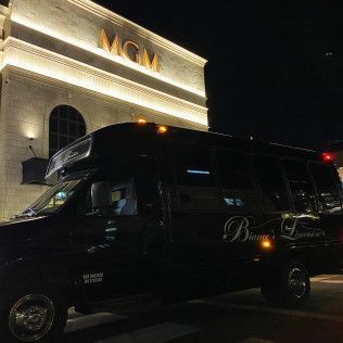 A black luxury passenger van parked at night in front of an MGM building with illuminated exterior signage.