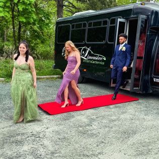 Two people in formal wear walk off a party bus onto a red carpet, while another stands nearby on a gravel path.