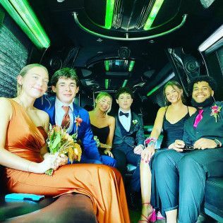 A group of six people in formal attire smiling inside a limousine with neon green accent lights.