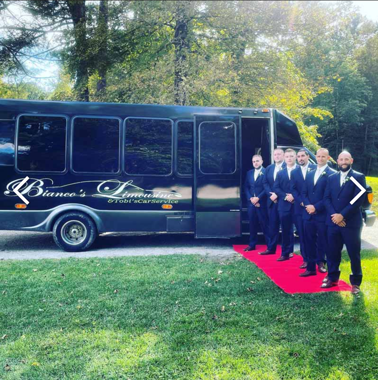 Six men in suits stand in a line on a red carpet by a black 