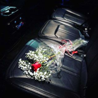 A single red rose surrounded by baby's breath, wrapped in clear plastic, resting on a black leather car seat.
