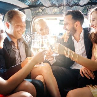 Four people in formal attire sit inside a limousine, laughing and holding glasses while making a toast.