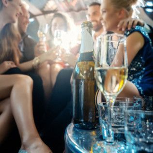 Close-up of a champagne bottle and glass in the foreground, with blurred people celebrating in the background.