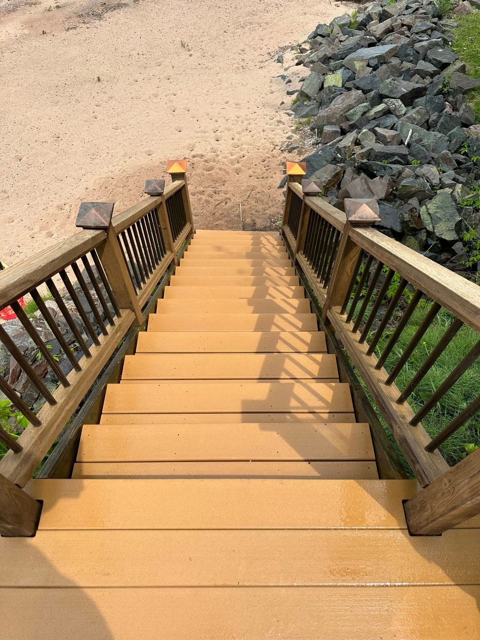 Wooden stairs descending to a rocky beach, with railings on both sides and green foliage on the right.