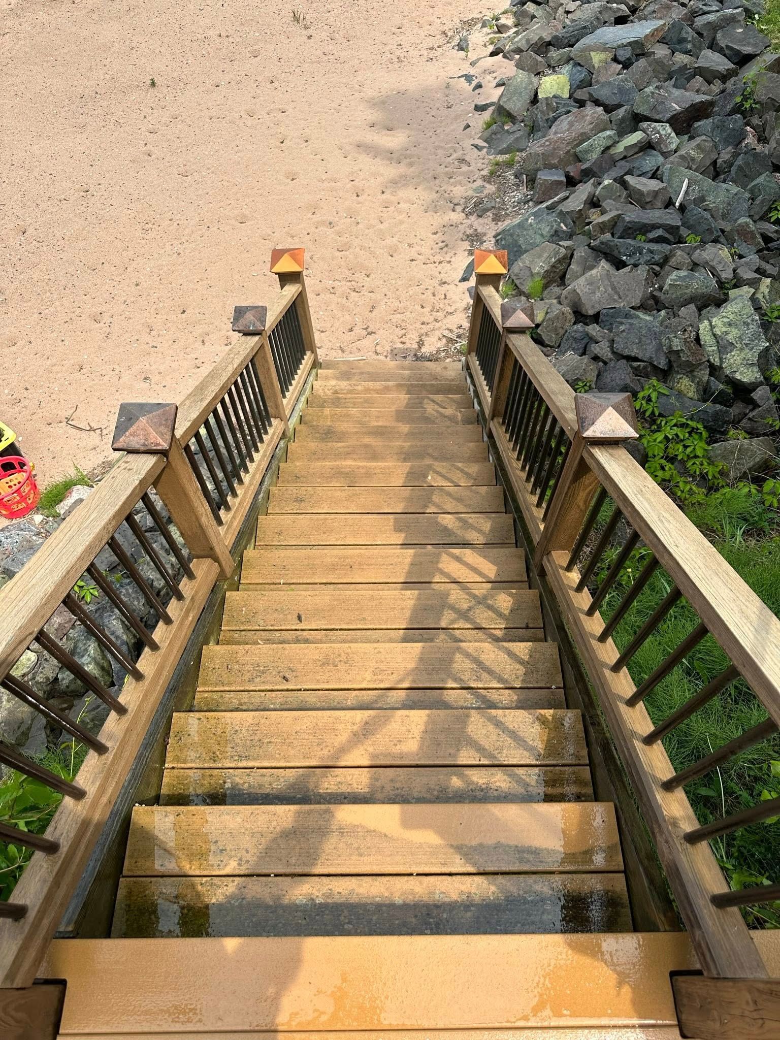Wooden staircase descending to a sandy beach, with railings and rocks on the right.