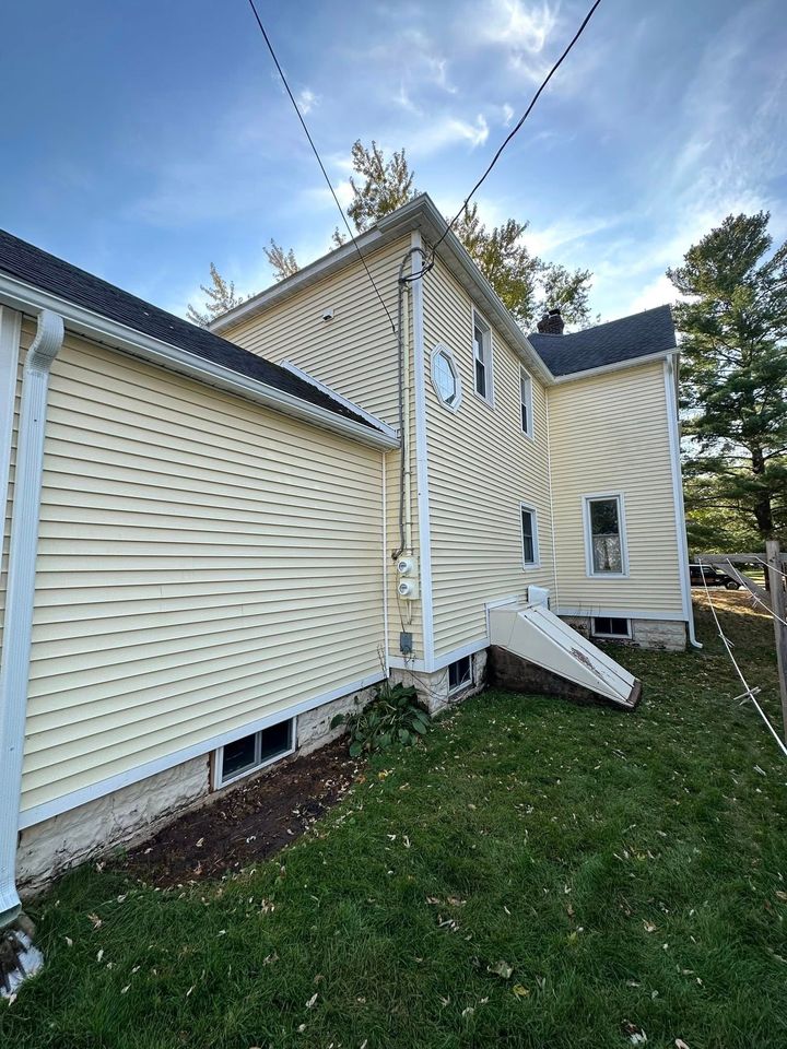 Damaged house siding with a large white canopy or screen torn loose on a grassy side yard