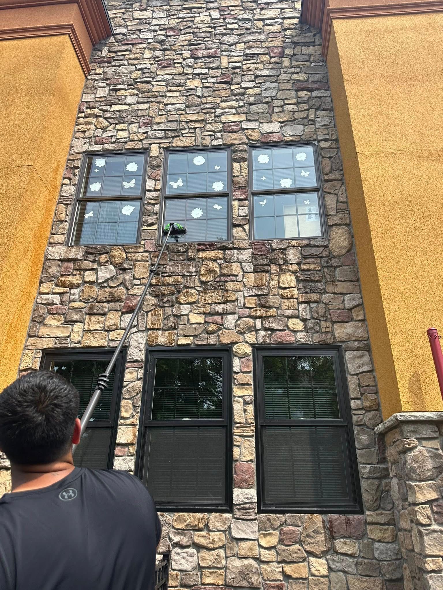 Stone building facade with black-framed windows and yellow side walls; a person stands in the foreground.
