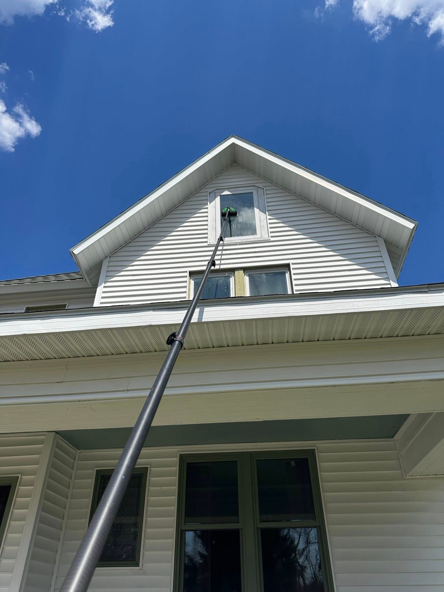 Extension ladder reaching up the side of a white house toward an upper gable under a blue sky.