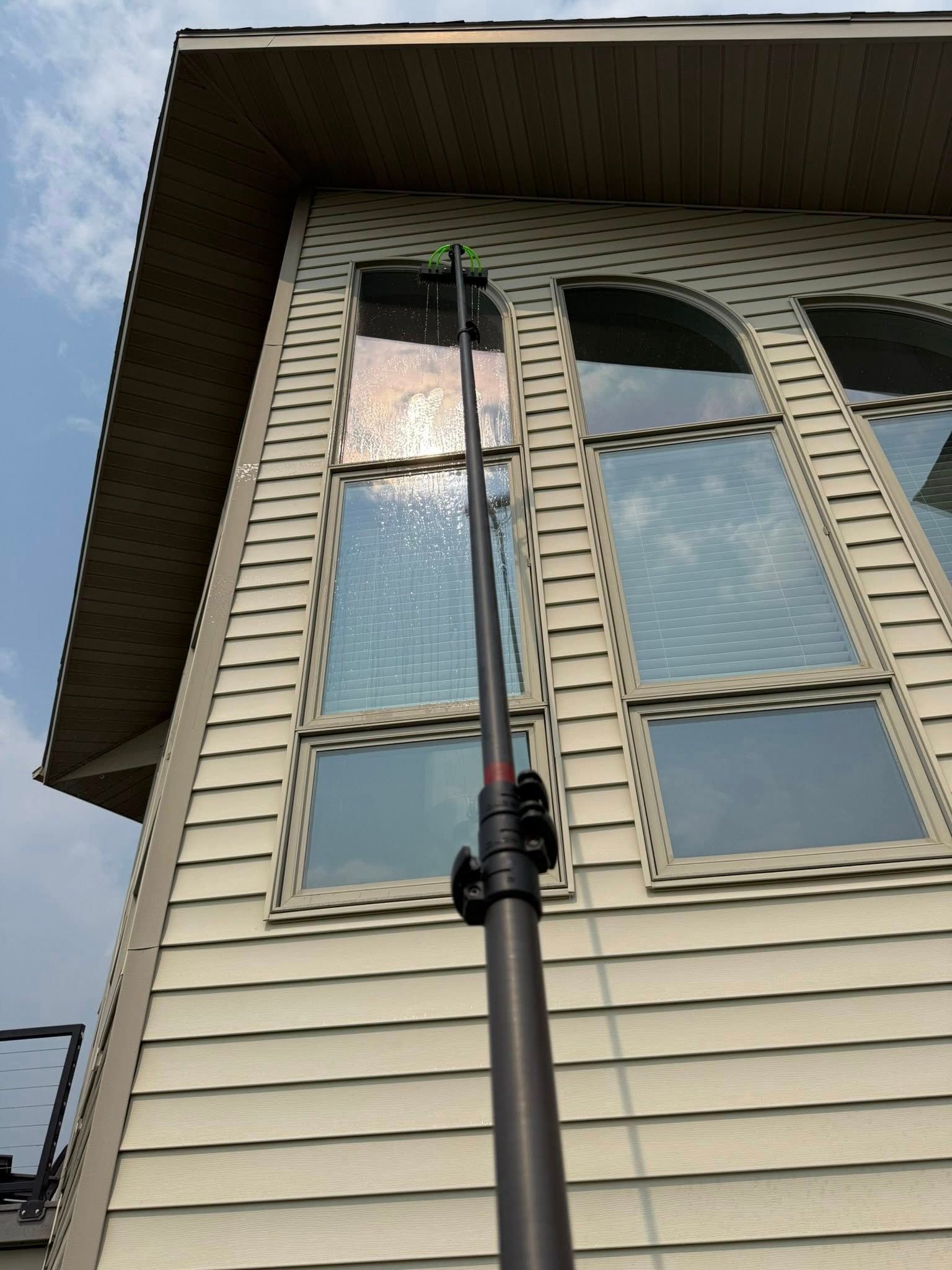 Telescoping pole reaching up to a second-story window on a beige house exterior