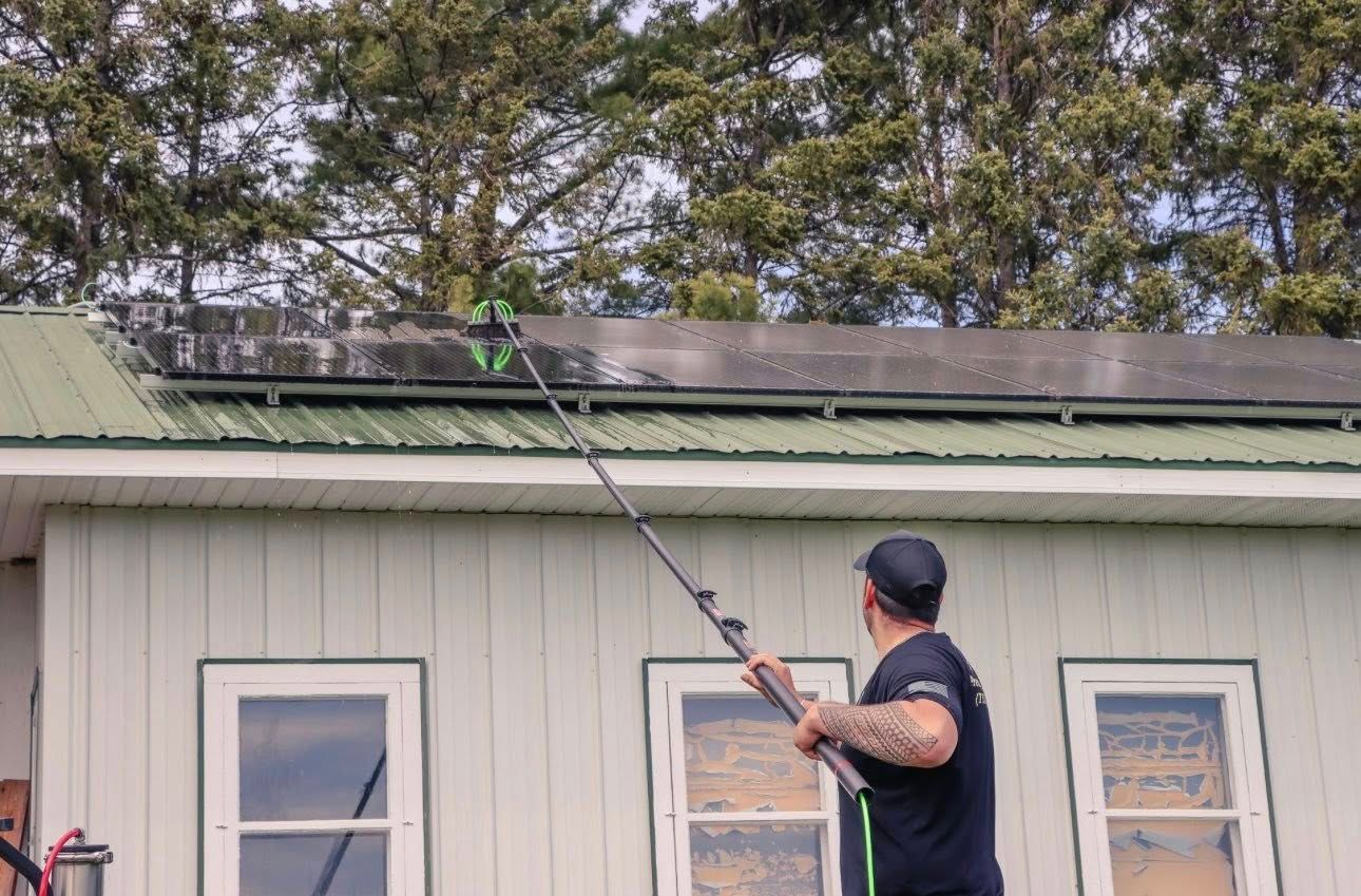 Person using a long pole to clean a green roof on a house with white siding.
