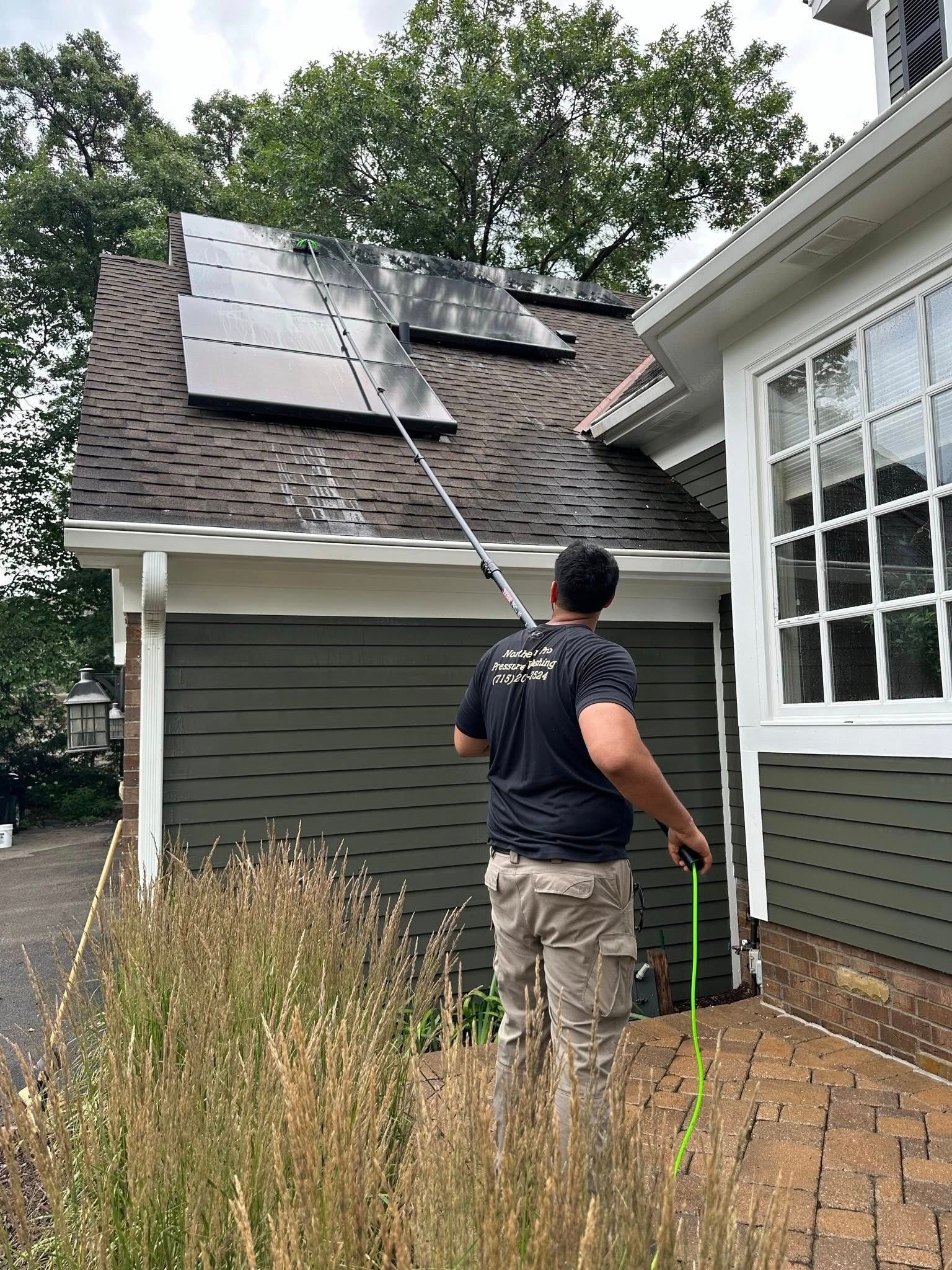 Worker inspecting solar panels on a gray-roofed house beside a white bay window.