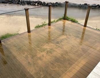 Rain-soaked wooden deck with metal posts beside muddy floodwater and rocks
