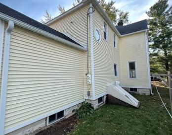 Side of a yellow house with white siding, small windows, and a white ramp leading to a side entrance.