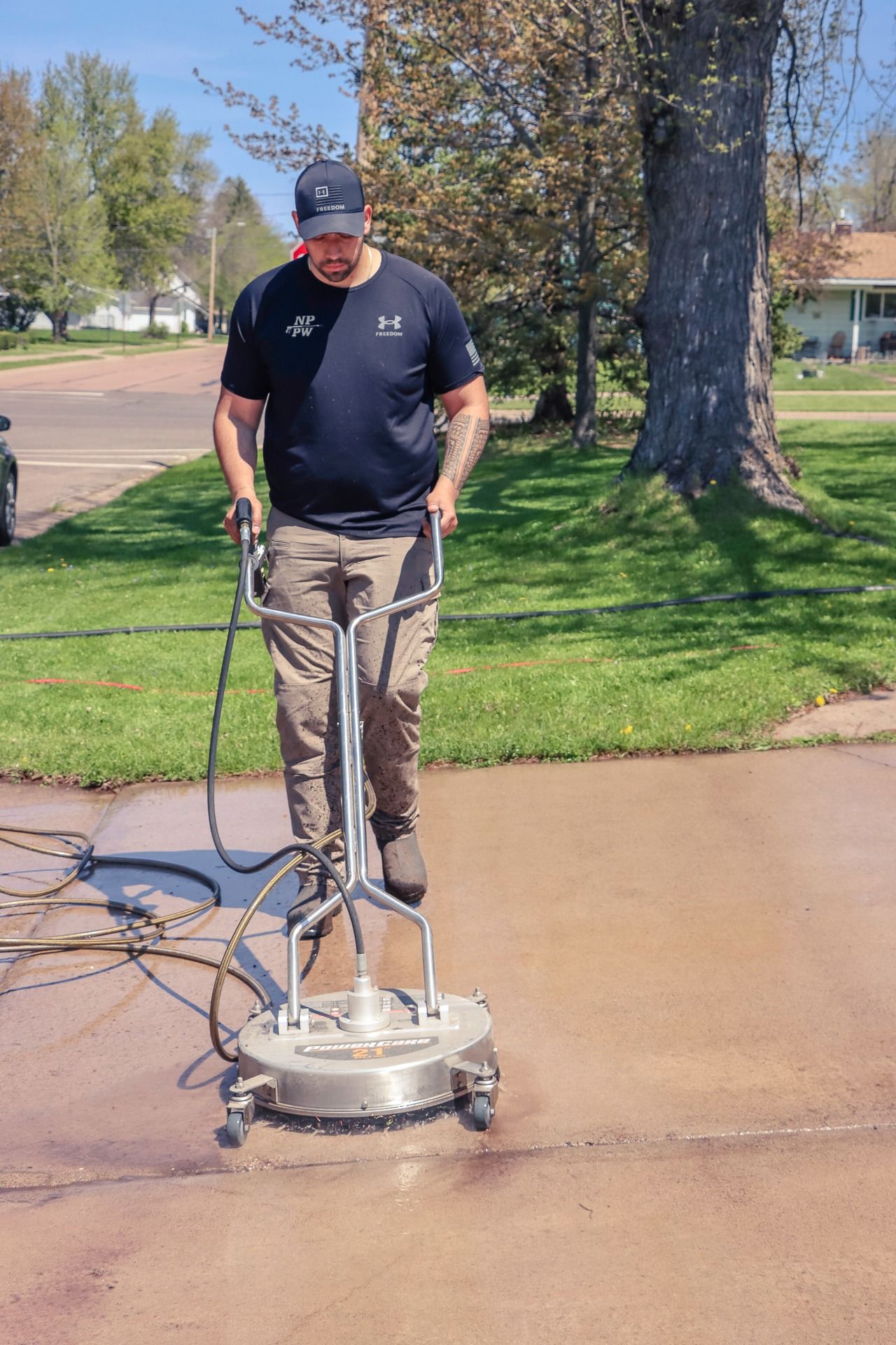 Worker power-washing a driveway with a surface cleaner in a residential yard