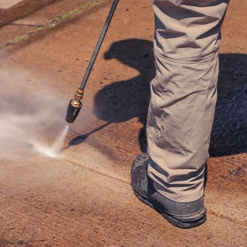 Person pressure-washing a concrete surface with a spray wand