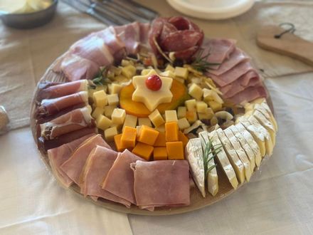 Planche de charcuterie composée de viandes tranchées, de fromages et de fruits disposés autour d'une sauce centrale ou d'une boule de fromage