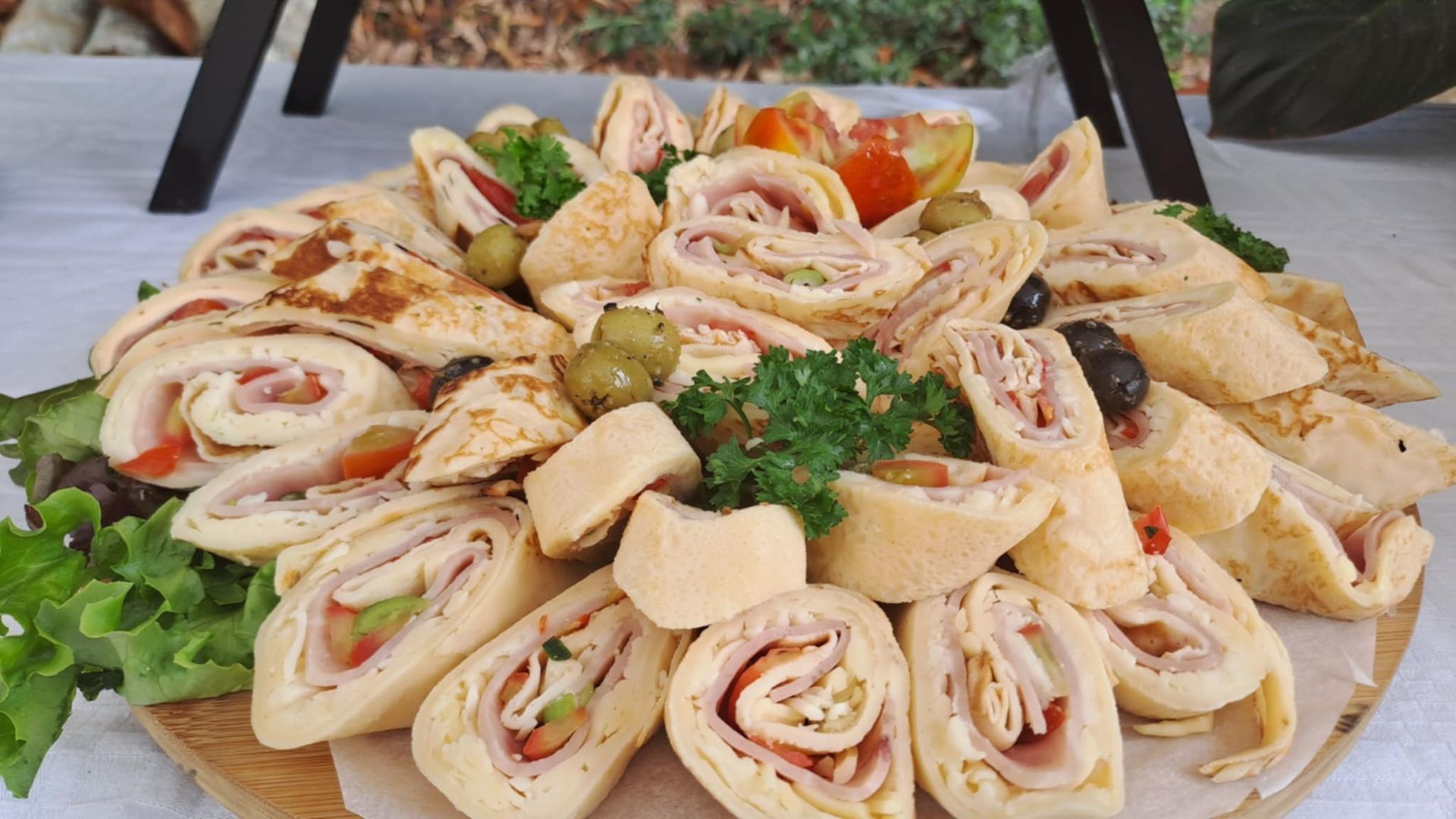 Plateau de roulés apéritifs aux herbes, tomates et fromage, présenté sur une table de service en extérieur.
