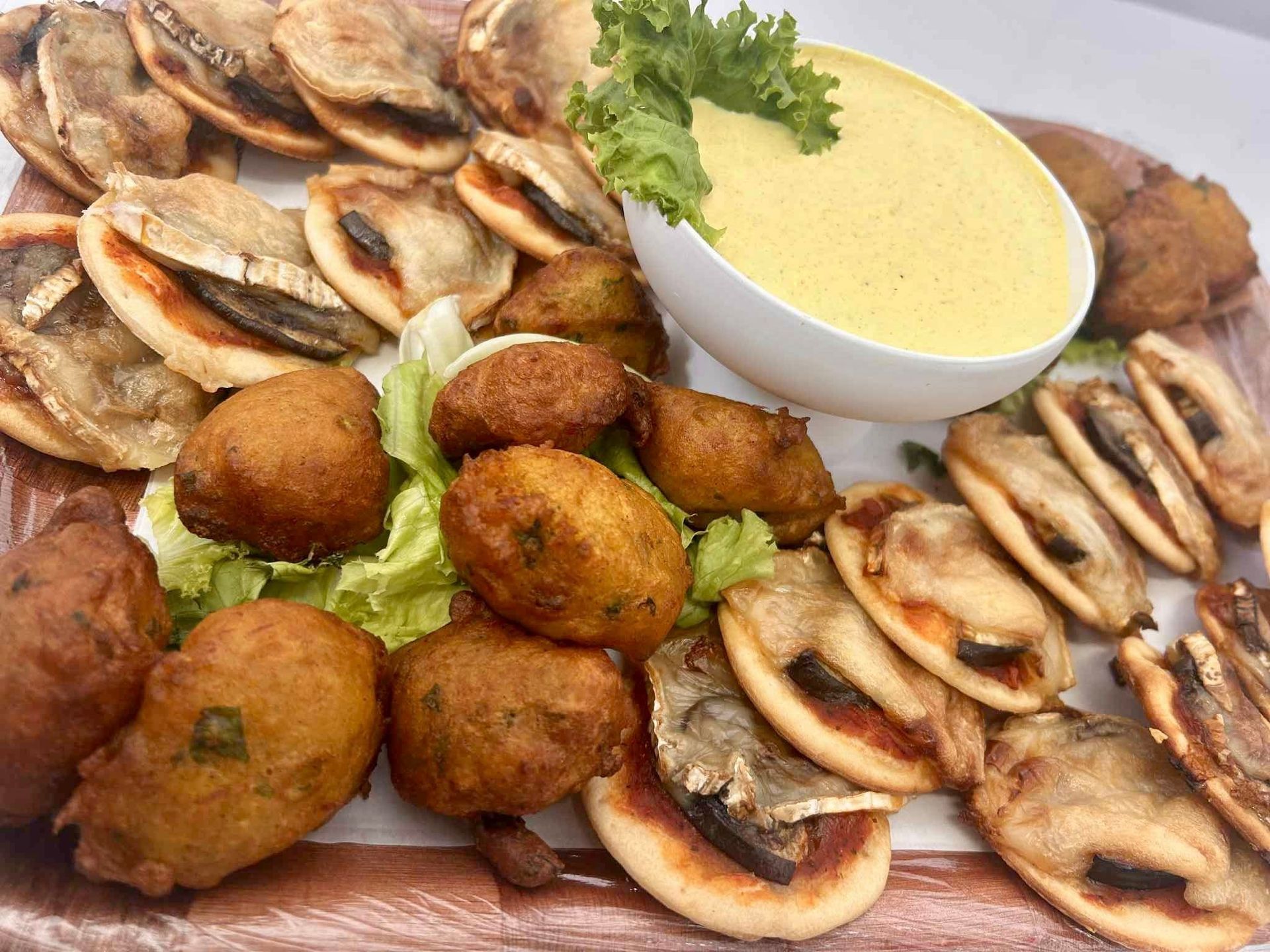 Assortiment de champignons frits et de beignets accompagnés d'un bol de sauce crémeuse.