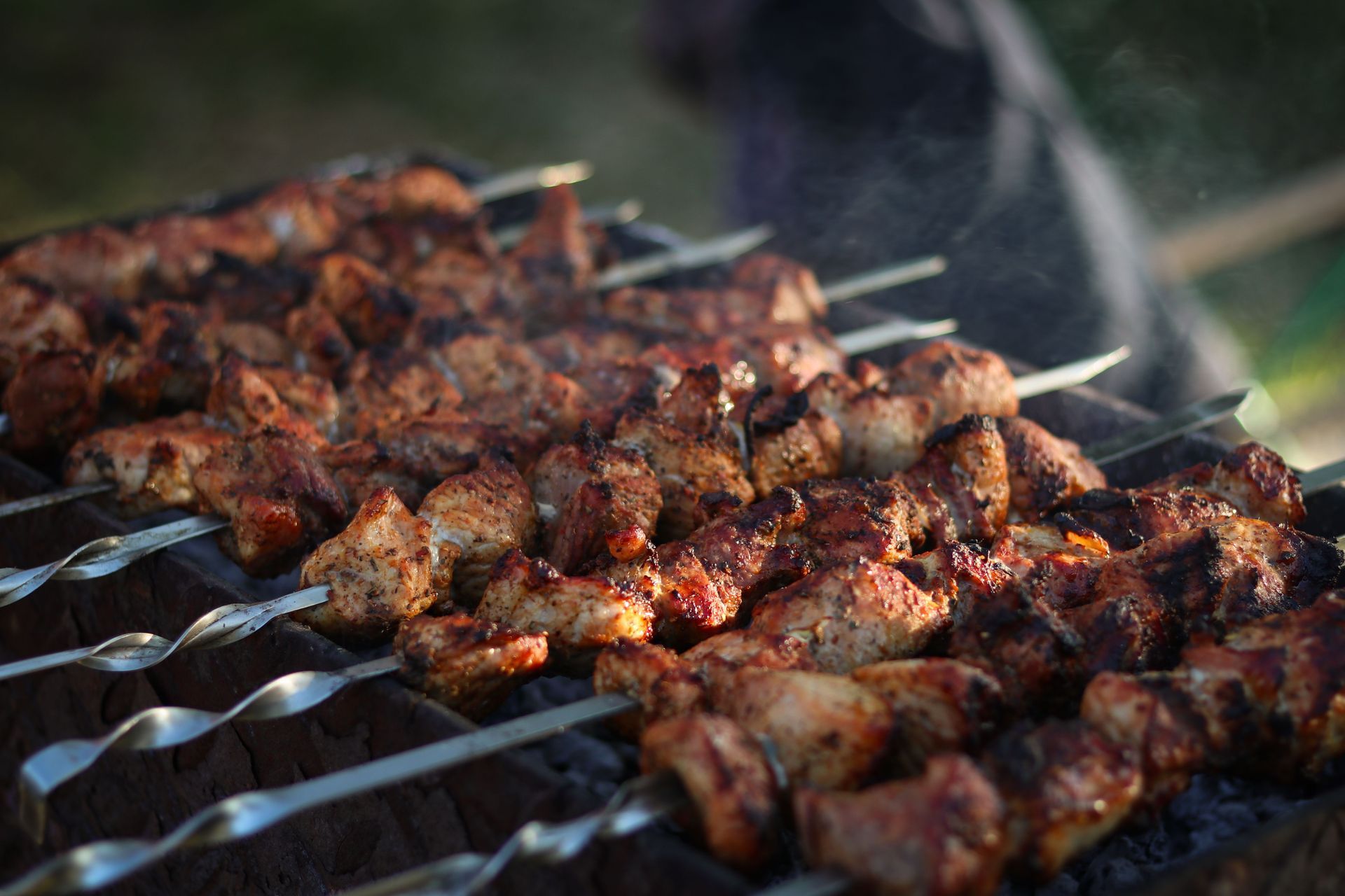 Brochettes de viande grillée carbonisée, cuisant à la flamme, d'où s'échappe de la fumée.