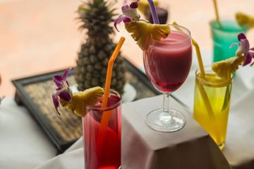 Des cocktails tropicaux colorés, garnis d'ananas, sont disposés sur une table à l'intérieur.