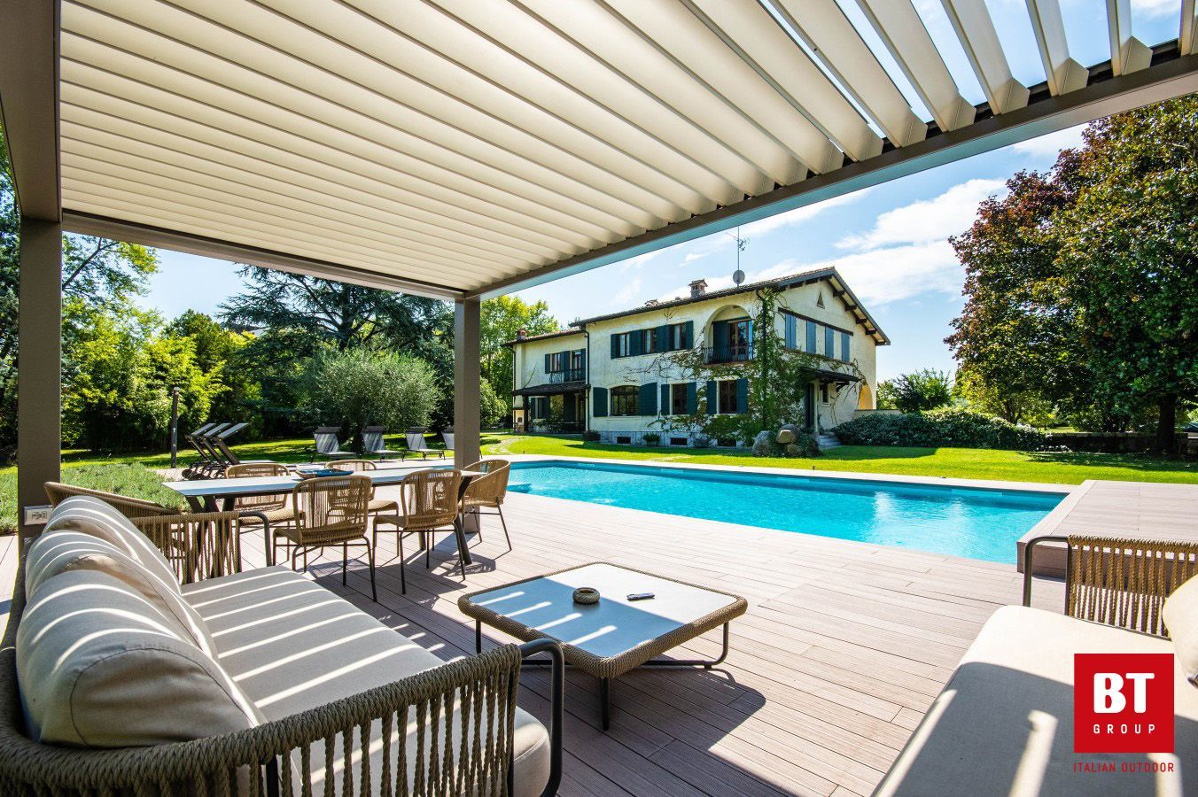 Un patio con pergolato e piscina sullo sfondo.