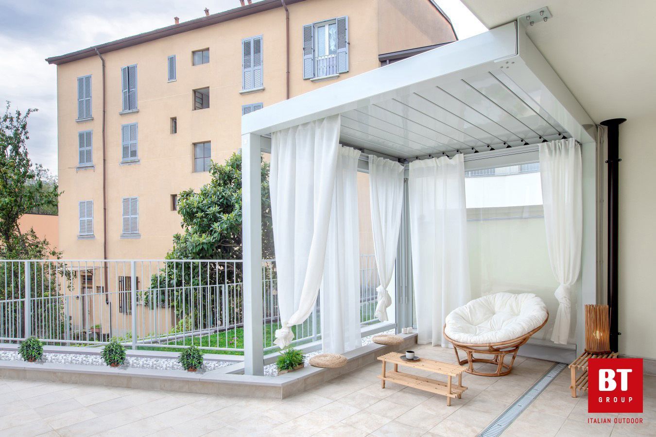 Un pergolato con tende bianche e una sedia davanti a un edificio.