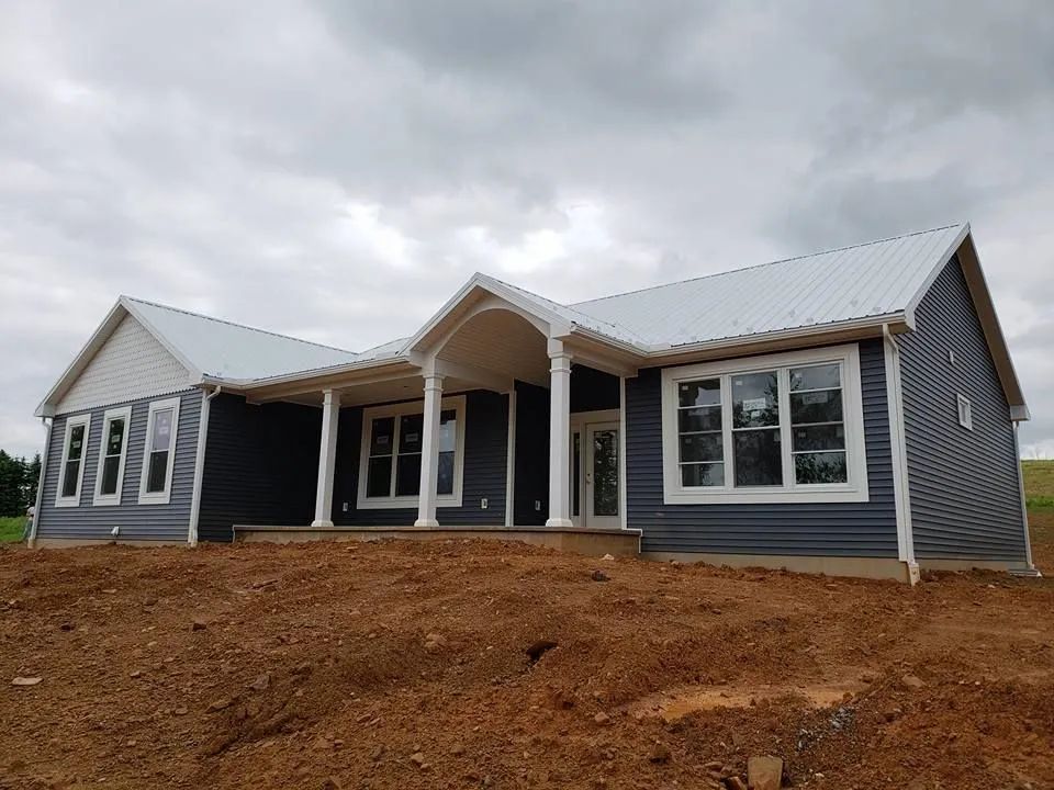 New gray house with white trim and front porch on a bare dirt lot under cloudy sky