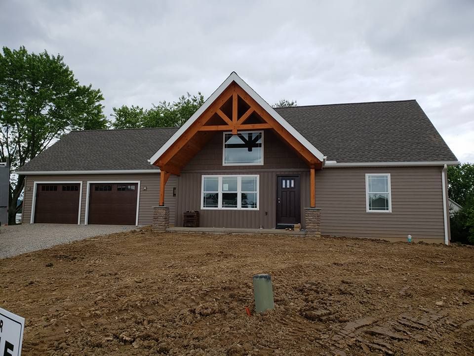 A newly built, one-story suburban home with brown horizontal siding, a timber-framed entryway, and two garage doors.