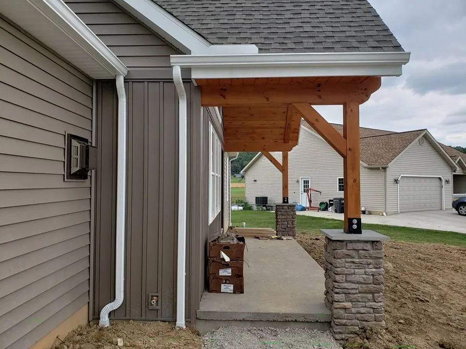 Covered front porch with wooden posts and stone columns beside a house exterior