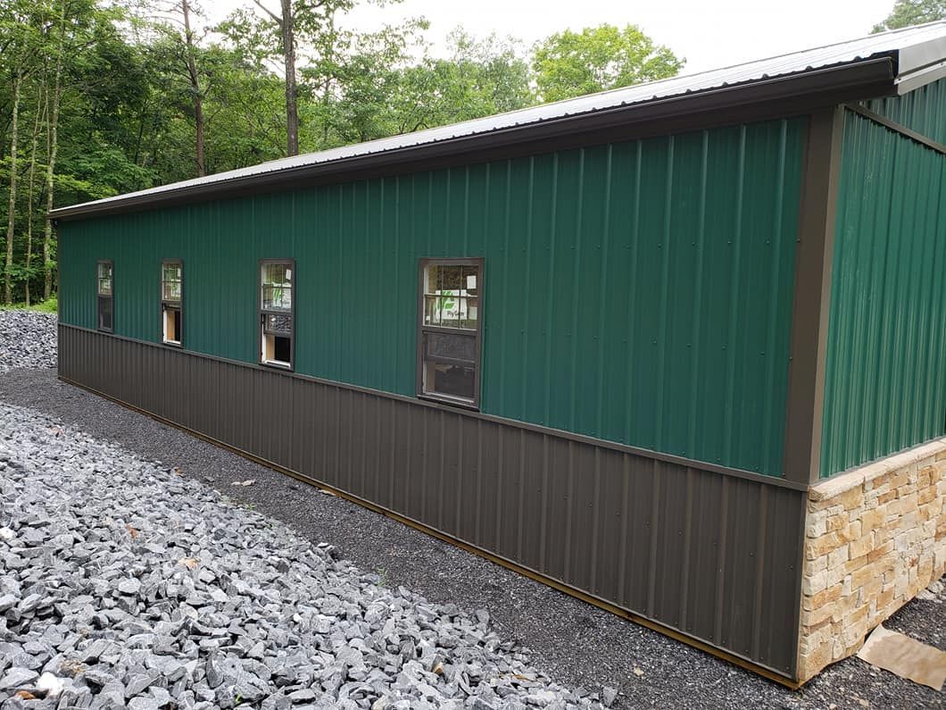 A side view of a metal building with green walls, a brown wainscot base, small windows, and a stone corner foundation.