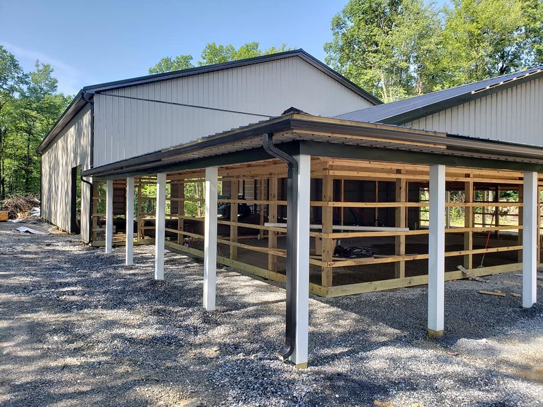 A metal building featuring a newly constructed, unfinished wooden frame porch supported by white posts over a gravel lot.