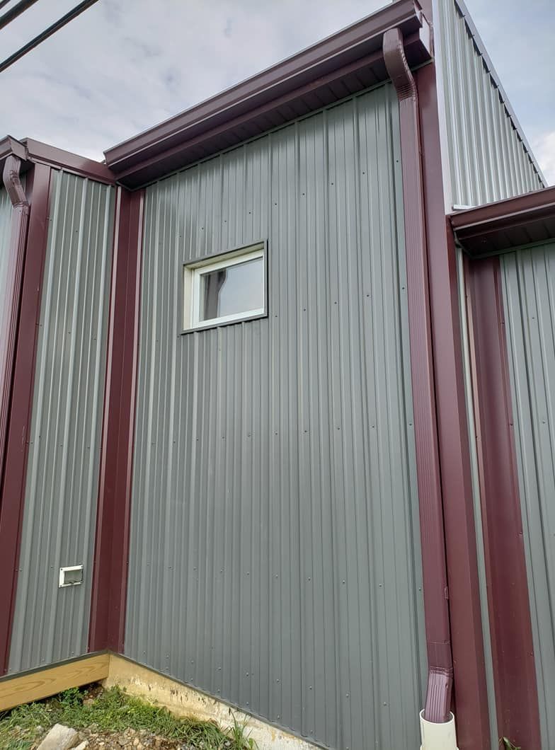 A close-up view of a building exterior with grey corrugated metal siding, dark red trim, and a small square window.